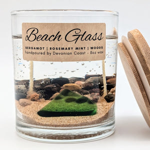 Candle in a glass jar with beach-themed design and wooden lid on a white background